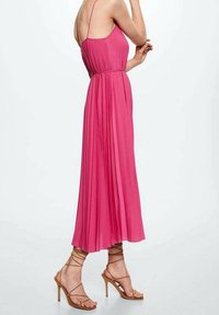 Robe maxi plissée rose avec une taille cintrée, des bretelles spaghetti et un bas fluide. Associée à des sandales à talons hauts nude à brides.