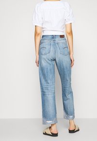Vaqueros de mezclilla azul claro con un corte relajado, con dobladillos deshilachados y dos bolsillos traseros. Combinados con un top blanco corto y sandalias tipo slid.