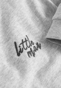 Szary sweatshirt z prążkowanymi mankietami. Na przodzie znajduje się ciemny, haftowany napis "little man". Miękka tekstura i swobodny krój.