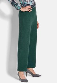Dunkelgrüne, strukturierte weit geschnittene Hose mit hoher Taille, kombiniert mit grauen Absatzschuhen, die einen glatten Stoff und klare Linien zeigen.