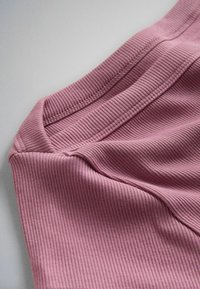 Primo piano di tessuto rosa morbido a coste con cuciture dettagliate lungo una cucitura, steso su una superficie chiara.