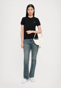 Black short-sleeve t-shirt, light blue flared jeans, white sneakers, holding a white curved handbag with gold accents and strap.