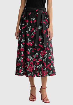 Falda midi negra con estampado de cerezas rojas y hojas verdes, botones delanteros, cinturón en la cintura, combinada con sandalias rojas de tacón alto y tiras.