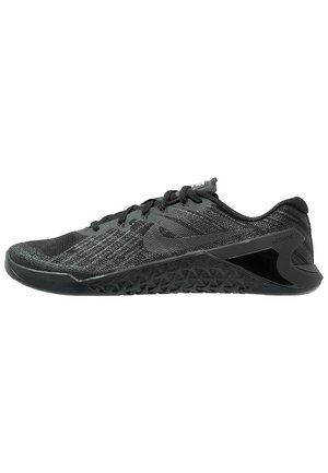 Zapatilla deportiva negra y gris con suela texturizada, parte superior de malla, cordones y un perfil bajo diseñada para entrenar o correr.