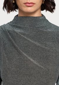 Schwarzes, schimmerndes Oberteil mit hohem Kragen, das mit drapiertem Stoff und glatter Textur überzeugt, und dezentes Schimmern sowie elegante Falten betont.