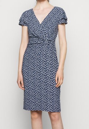 Frau trägt ein knielanges dunkelblaues Kleid mit kleinem weißem Blumenmuster, kurzen gerafften Ärmeln und V-Ausschnitt.