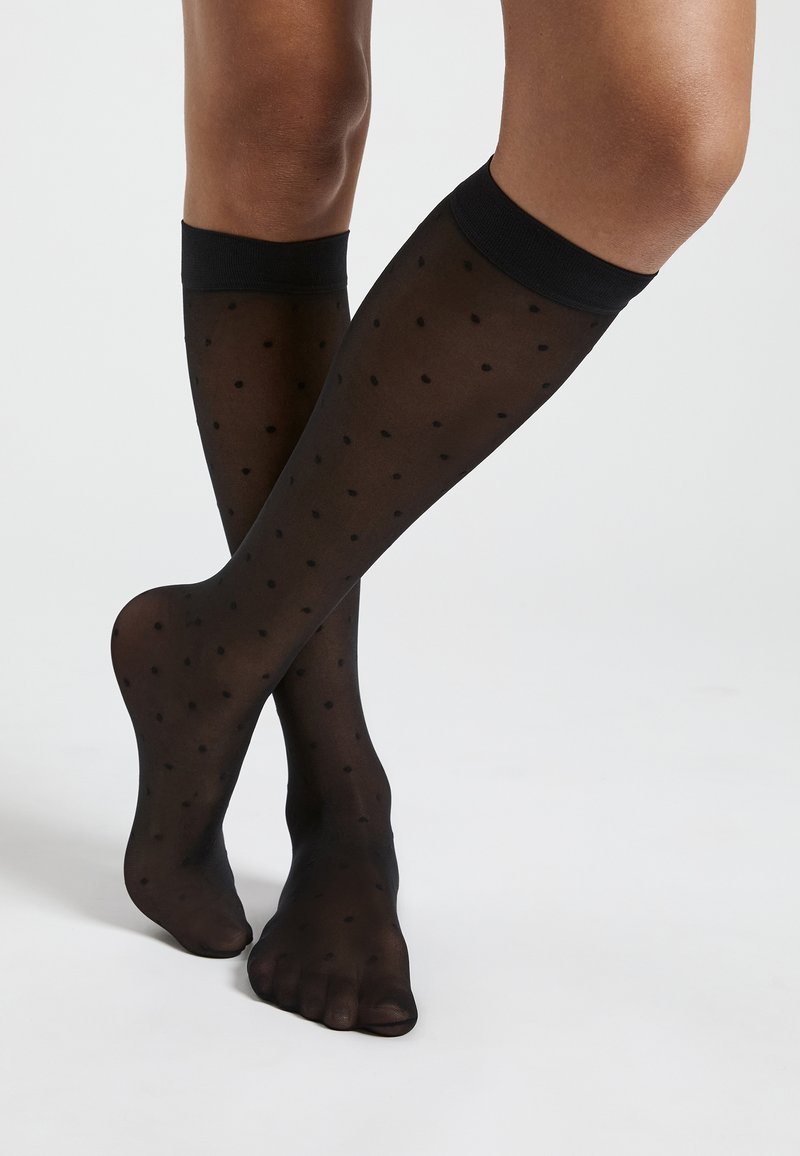 Schwarze kniehohe Socken aus transparentem Material mit einem Punktmuster und einem einfarbigen schwarzen Band oben. Die Zehen sind frei.
