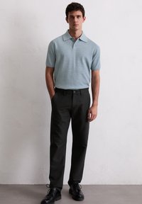 Hellblaues kurzärmeliges Polohemd aus strukturiertem Stoff, kombiniert mit schwarzen Hosen. Schwarze Schuhe und ein taillierter Schnitt vervollständigen das Outfit.