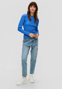 Blaues geripptes Langarmoberteil kombiniert mit hellen, locker sitzenden Jeans und weißen Plateauschuhen. Einfaches Design ohne sichtbare Muster.
