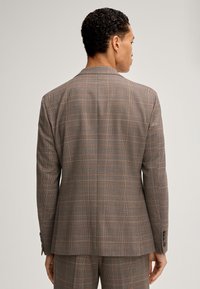 Szary garnitur w kratę z pomarańczowymi akcentami, z klasycznym kołnierzem, usztywnionymi ramionami i zapinanymi mankietami. Dopasowany krój, gładka tekstura.