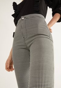 Black and white checked high-waisted pants with front pockets and a silver button closure, featuring a smooth texture and slim fit.