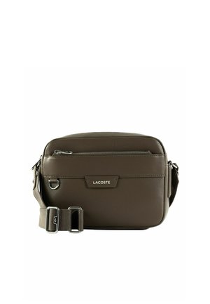 Petit sac bandoulière rectangulaire en cuir marron avec poche zippée à l'avant, sangle réglable et plaque logo Lacoste centrée sur le devant.
