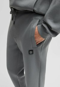 Grijze sweatpants met een slim fit, een tailleband met trekkoord, zijzakken en een zwart "HUGO" logo patch op de linker-dij. Zachte textuur.