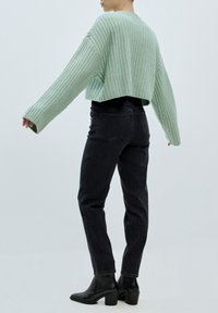 Mátově zelený žebrovaný oversize svetr s dlouhými rukávy, spárovaný s černými džínami s vysokým pasem a černými kotníkovými botami na blokovém podpatku.