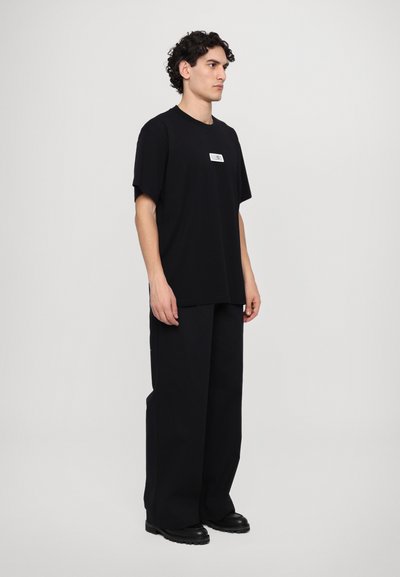 T-shirt noir oversize avec des manches courtes, arborant une petite étiquette graphique sur la poitrine. Associé à un pantalon noir ample et des bottes noires massives.