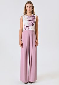 Pantaloni a gamba larga di un leggero rosa abbinati a un top senza maniche bianco con una stampa floreale in delicate tonalità viola. Texture del tessuto morbida.