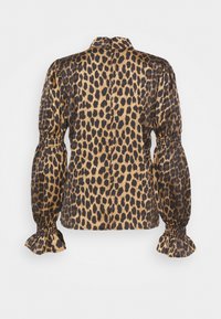 Blouse en imprimé léopard, tissu soyeux, dos à boutons, manches bouffantes avec poignets élastiques, motif marron et noir sur fond beige.