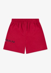 Shorts rouges en coton avec une taille élastique. Ils présentent un logo noir sur le côté gauche et une texture lisse avec un design simple.
