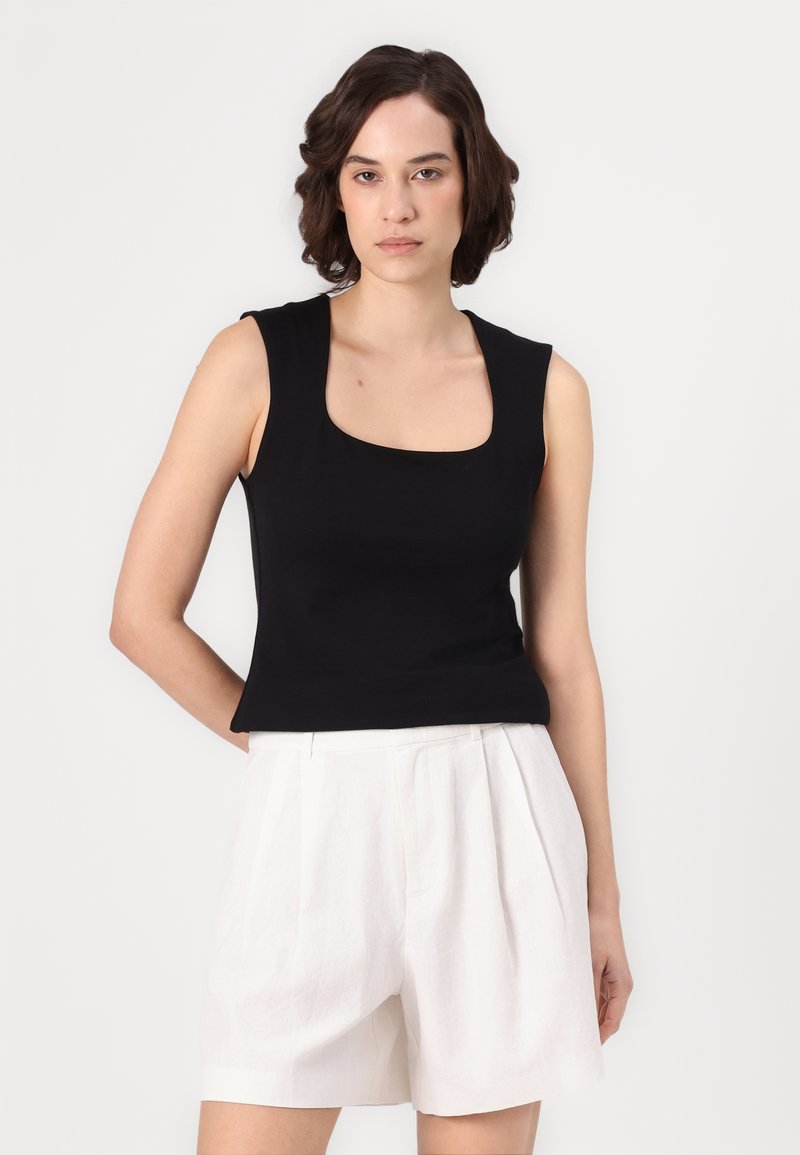 Czarny top bez rękawów o kwadratowym dekolcie, wykonany z gładkiego materiału, zestawiony z białymi, plisowanymi szortami. Minimalistyczny design, dopasowany krój.