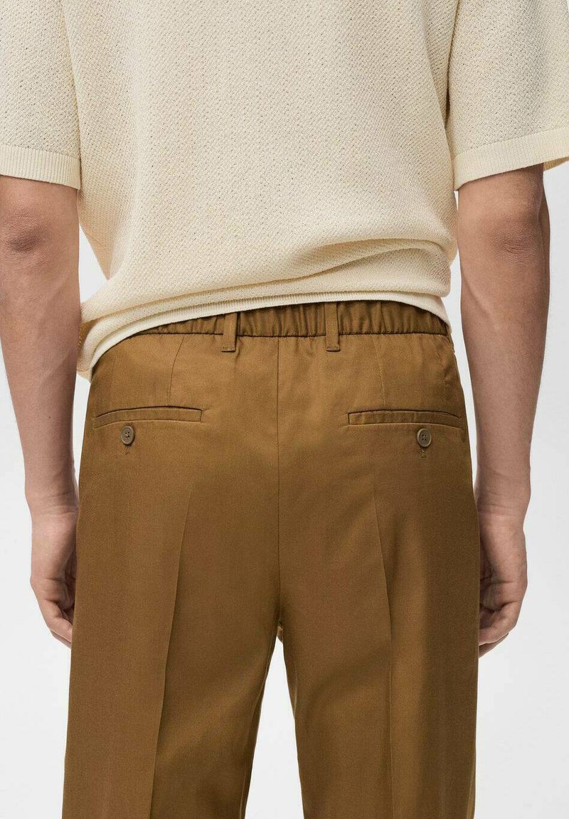 Pantaloni marroni con vita elastica, due tasche posteriori con bottoni, abbinati a un top in maglia crema testurizzato, che presenta una vestibilità rilassata e design plissettato.