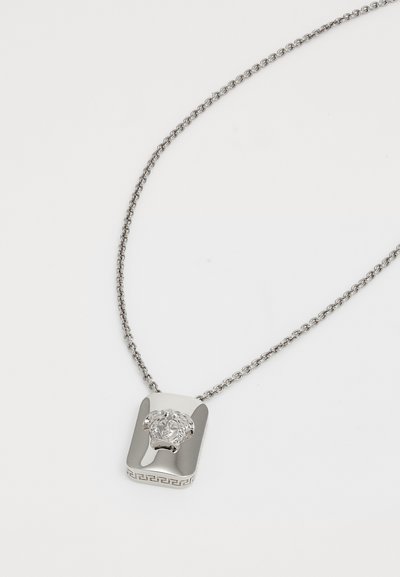 Collier en argent avec un pendentif rectangulaire, présentant un motif de tête de lion et un motif grec en bas. La chaîne est torsadée.