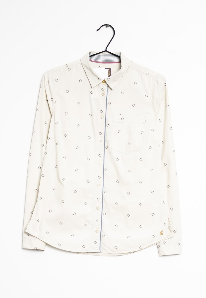 Chemise blanche à manches longues avec petits motifs circulaires, une poche poitrine avant et un col, suspendue sur un cintre noir sur un fond blanc.
