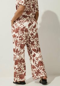 Blommönstrade vida byxor i kräm och rostfärger, med ribbad textur och sidofickor. Styling med platta sandaler.