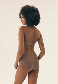 Brązowy stanik z żebrowanej dzianiny z szerokimi ramiączkami i regulowanym zapięciem na haftkę, w komplecie z dopasowanymi krótkimi spodenkami o żebrowanej strukturze. Gładka tekstura.