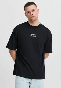 Zwarte katoenen T-shirt met korte mouwen, ronde halslijn, met witte tekst "Acties Beslissingen" gecentreerd op de voorkant. Casual ontwerp.