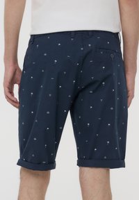 Pantaloni corti blu navy con orlo arrotolato, caratterizzati da piccole palme bianche e schemi geometrici. Realizzati in un tessuto leggero con un design casual.