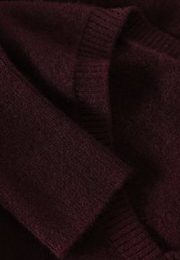 Maglione bordeaux lavorato a maglia con polsini e orlo a coste, realizzato in un materiale morbido e strutturato, con un aspetto leggermente peloso.
