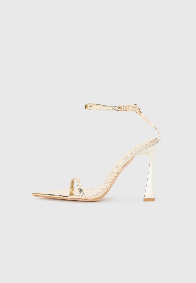 Gold high-heeled sandal with a pointed toe and slender ankle strap. Features a glossy finish and a sculpted geometric heel.