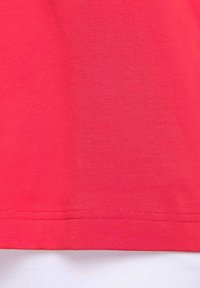 T-shirt aderente in cotone rosa vivace, texture liscia, maniche corte, orlo irregolare, con dettaglio di cucitura lungo il bordo inferiore.