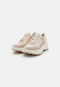 Beige sportsko som har en blanding av glatt skinn og semsket skinn. Kraftig hvit såle med et teksturert mønster og subtile logopregninger på sidene.