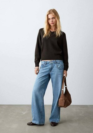 Pull en maille foncée, jean large bleu clair, sac à épaule marron et chaussures marron, sur un fond neutre.