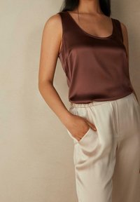 Top sin mangas de satén marrón combinado con pantalones de satén crema de corte holgado, con cinturilla elástica y bolsillos laterales. Textura suave y diseño elegante.
