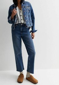 Veste en denim à boutons, associée à une chemise rayée boutonnée. Jean taille haute à jambes droites et sabots marron complètent la tenue.