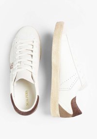 Sneakers bianche con tomaia in pelle liscia, tallone in pelle marrone testurizzata e suola in gomma beige. Presentano lacci piatti e perforazioni sui lati.