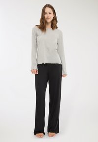 Maglietta grigia a maniche lunghe con orlo scallop abbinata a pantaloni neri larghi. Texture morbide, design casual e scarpe aperte visibili.