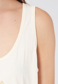 Camiseta sin mangas blanca con un escote amplio y ribetes acanalados. Tejido suave y ligero con una textura suave. Sin patrones ni acentos visibles.