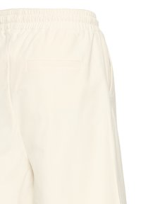 Pantalon couleur crème avec taille élastique, présentant une poche passepoilée à l'arrière et une poche latérale sur le côté droit.
