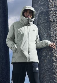 Lichtgrijze, gewatteerde jas met een capuchon, ritsluiting en verstelbare koordjes, gecombineerd met zwarte sweatpants met zakken en een logo.