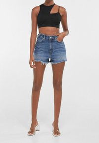 Svart ribbade cropped topp med asymmetrisk skärning, kombinerad med högmidjade denimshorts med fransade kanter och en ljus tvätt. Klara klacksandaler.