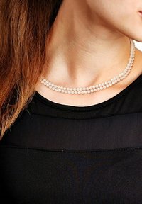 Collier de perles à deux brins, comprenant de petites perles translucides dans une teinte douce et pâle. Porté sur un top noir, texture lisse.