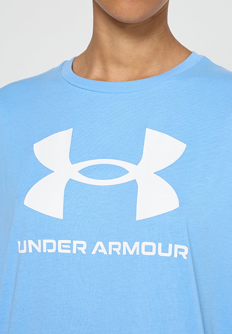 Jasnoniebieska koszulka bawełniana z dużym białym logo Under Armour oraz tekstem poniżej. Okrągły dekolt, krótkie rękawy i luźny krój.