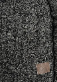 Grijs en zwart gebreid sweater met een dik kabelbreipatroon. Inclusief een bruine leren label met het woord "Solid."