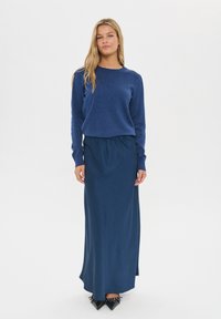 Tums zils adīts džemperis un atbilstoša gara svārku. Gluda tekstūra ar pieguļošu jostu uz svārkiem. Nēsājams ar melnām, norādītām kurpēm.