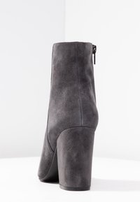 Bottine en suede gris avec un talon bloc haut, texture lisse et fermeture éclair sur le côté. Design minimaliste avec une silhouette épurée.