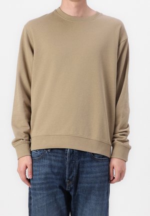 Beżowy sweter z długim rękawem i okrągłym dekoltem, noszony z niebieskimi dżinsami, przedstawiony od szyi do bioder na białym tle.