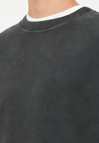 Dunkelgrauer Sweatshirt mit Rundhalsausschnitt, der eine strukturierte Oberfläche und einen kontrastierenden weißen Innenkragen aufweist. Glatte Stoffoberfläche.
